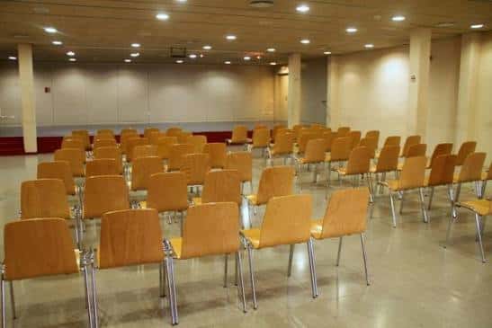 Sala de actos interior con sillas naranjas dispuestas para conferencias o eventos culturales