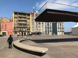 Plaza de Santiago López con la pasarela moderna de La Grapa y bancos curvos en primer plano