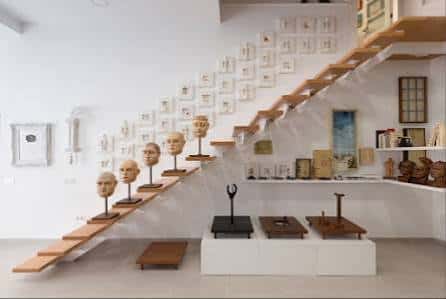 Interior del Desván Blanco mostrando una escalera flotante y una exposición de arte con bustos en la pared