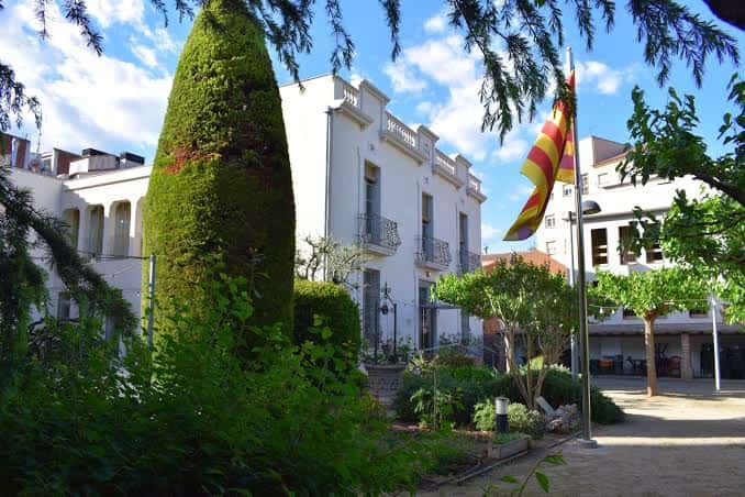 Vista exterior del Llar d'Avis de la Parròquia de Sant Cugat con bandera catalana y jardines