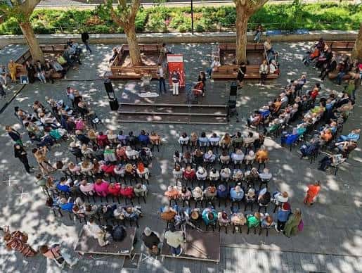 Evento cultural en la Plaza de la Memoria con público sentado en sillas y escenario al aire libre