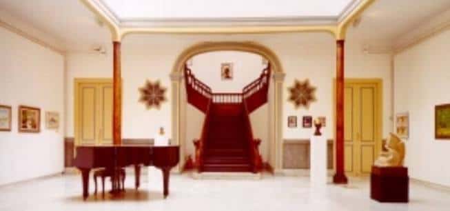 Interior del hall principal con escalera de madera, piano y obras expuestas
