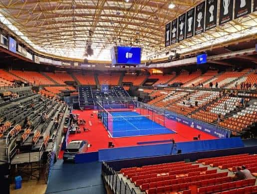 Interior del pabellón configurado para un evento de pádel con cancha azul y gradas naranjas