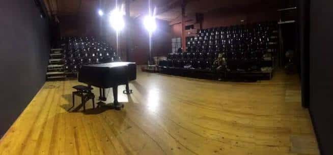 Escenario del teatro con un piano de cola y las butacas de fondo bajo iluminación