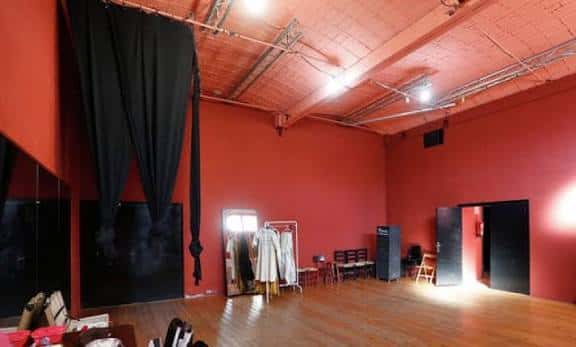 Sala de ensayo o espacio alternativo del teatro con paredes rojas y cortinas negras