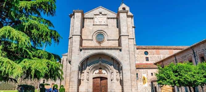 Vista frontal del monasterio bajo cielo azul, destacando su arquitectura gótica y detalles escultóricos