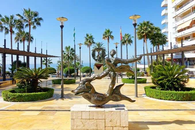 Escultura de delfines en el paseo marítimo del parque con palmeras al fondo