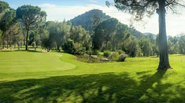 Hoyo del campo de golf rodeado de árboles y colinas al fondo