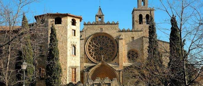Vista panorámica del monasterio con torres y rosetón, enmarcado por árboles