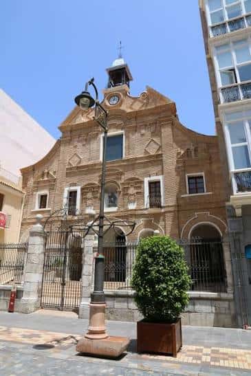 Vista exterior de la Iglesia de Nuestra Señora del Carmen en Cartagena, con su fachada de ladrillo y campanario bajo un cielo despejado