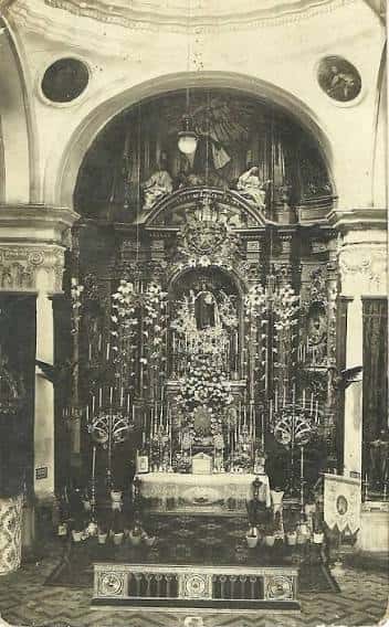 Interior histórico de la iglesia mostrando el altar principal con decoración barroca y flores, capturado en fotografía antigua en blanco y negro