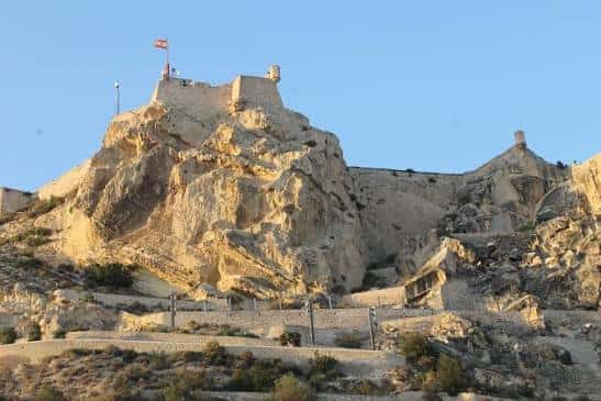 Vista panorámica del Castillo de Santa Bárbara sobre la montaña con bandera española
