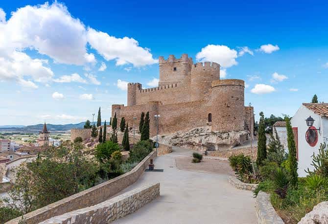 Fachada principal del castillo con torres medievales y camino de acceso