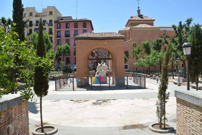 Vista frontal de la plaza con el arco de ladrillo y la estatua central decorada con banderines festivos