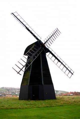 Molino de viento Beacon Mill con fondo de cielo nublado y paisaje costero al fondo