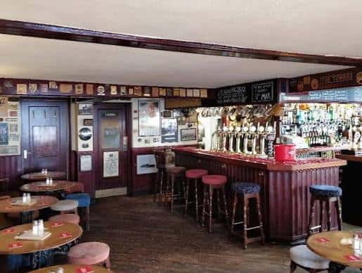 Interior tradicional del pub con barra de madera, grifos de cerveza y mesas redondas