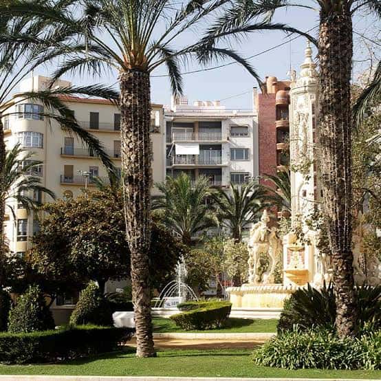 Plaza de los Luceros enmarcada por palmeras, mostrando la fuente y edificios residenciales al fondo