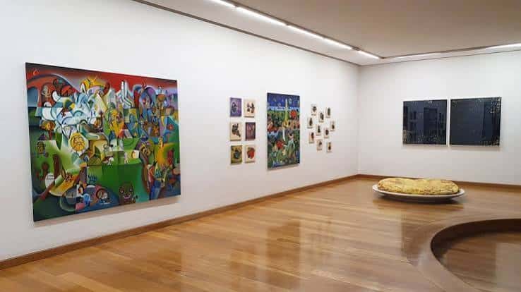 Sala de exposición con obras de arte abstracto y suelo de madera