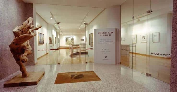 Entrada principal con escultura de madera y cartel de exposición