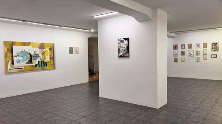 Sala de exposición con obras enmarcadas y suelo de baldosas grises