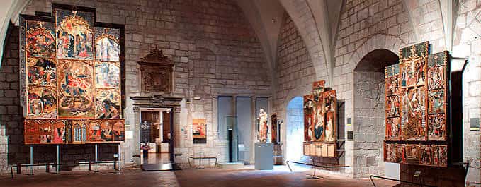 Interior del museo con grandes retablos medievales expuestos en salas de bóveda de piedra