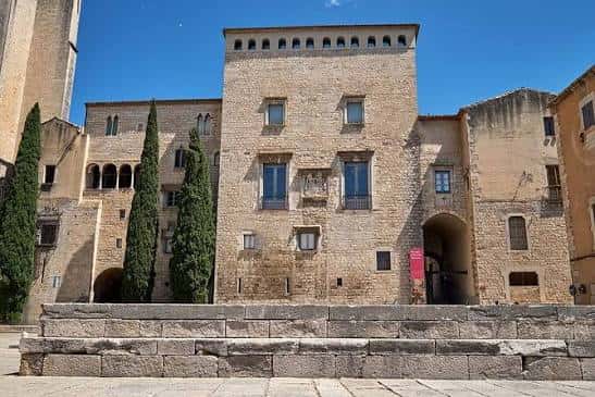 Fachada principal del museo con entrada arqueada y cipreses bajo cielo azul