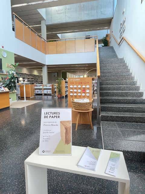 Hall principal de la biblioteca con escalera, exposición 'Lectures de Paper' y zona de lectura