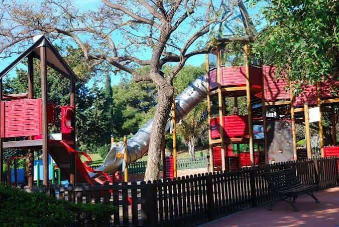 Área de juegos infantiles con estructuras de madera y toboganes en el parque