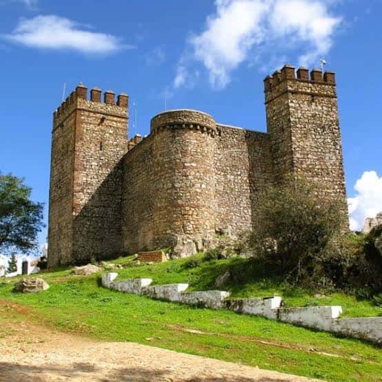 Vista frontal del castillo con sus dos torres cuadradas y muros de piedra en un día soleado