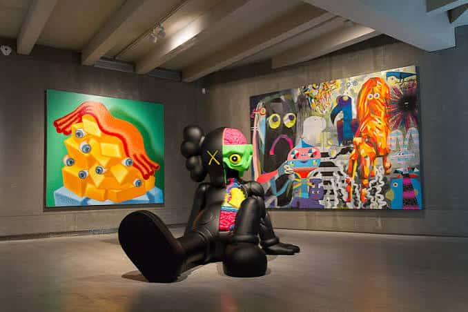 Espacio expositivo con escultura de KAWS y cuadros coloridos de arte urbano