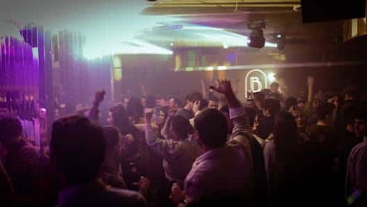 Multitud de asistentes con las manos en alto bajo luces de discoteca en Sala B