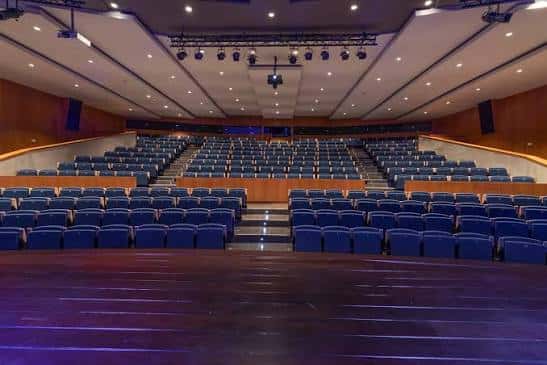 Vista general del auditorio vacío con butacas azules y escenario iluminado