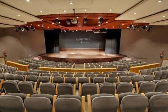 Interior del auditorio con butacas grises y escenario principal