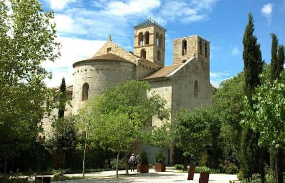 Fachada principal del monasterio rodeada de árboles bajo cielo azul