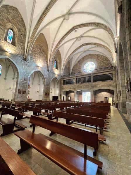 Interior de la iglesia con bóvedas de crucería, bancos de madera y luz natural