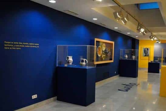 Sala de exposiciones del museo con vitrinas de cerámica y paredes azules