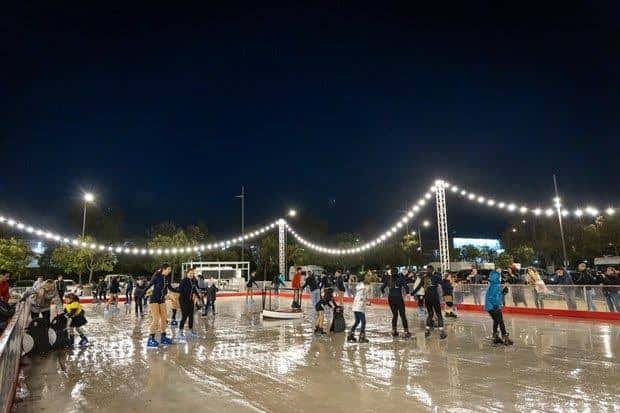 Pista de hielo nocturna con luces decorativas y personas patinando