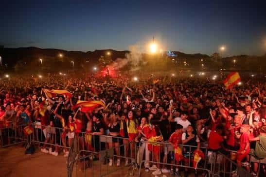Multitud celebrando en la plaza con banderas españolas y fuegos artificiales