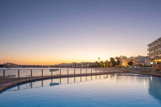 Vista de la piscina del hotel al atardecer con el mar de fondo