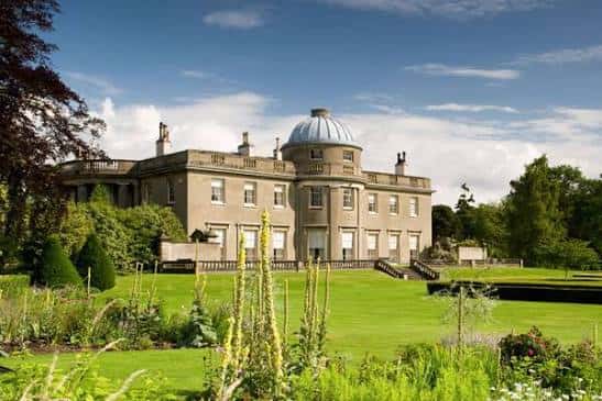 Vista exterior de Scampston Hall con jardines bien cuidados y cielo despejado