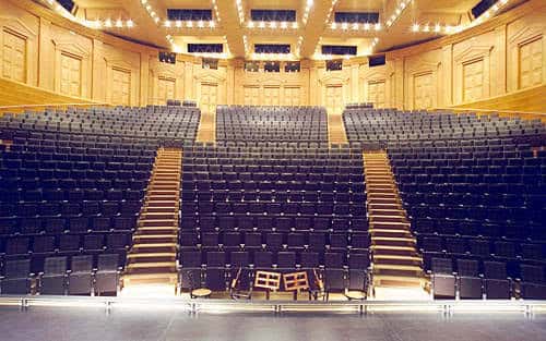 Interior del auditorio principal con butacas oscuras dispuestas en gradas y escenario iluminado