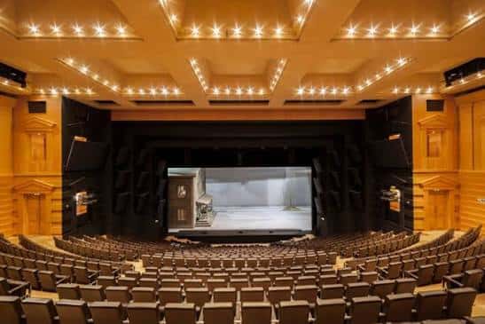Vista panorámica del auditorio desde la parte trasera, mostrando el escenario con escenografía y techo con iluminación decorativa