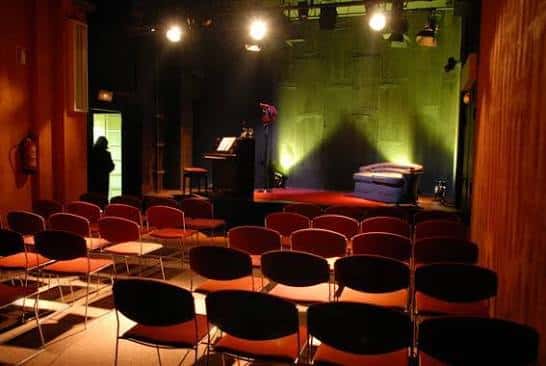 Escenario del Teatre Gaudí con iluminación verde y mobiliario para presentación o conferencia