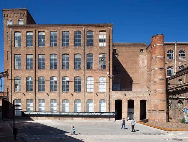Fachada principal de la fábrica con chimenea y personas caminando