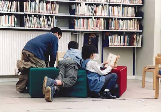 Escena de lectura infantil en la biblioteca con niños en cojines coloridos