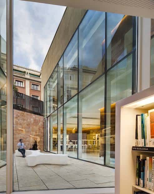 Interior luminoso de la biblioteca con grandes ventanales de cristal y zona de lectura moderna