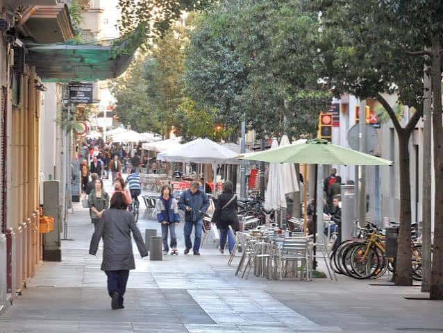 Vista diurna de Carrer de Blai con terrazas de restaurantes y peatones caminando