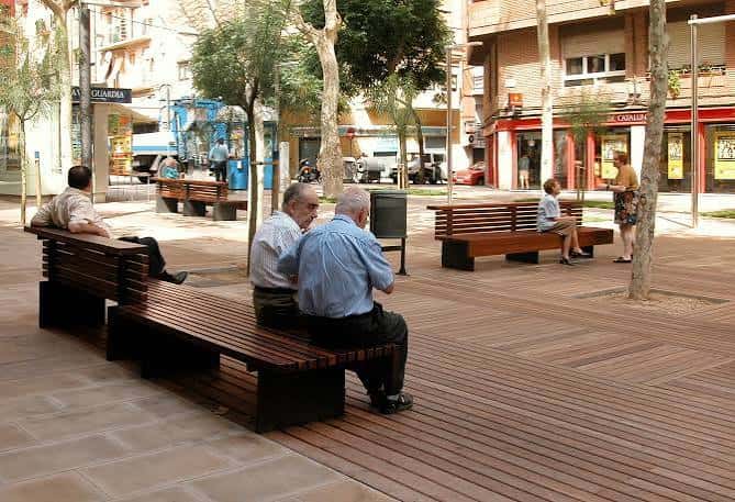Vista de la plaza con bancos de madera y personas descansando