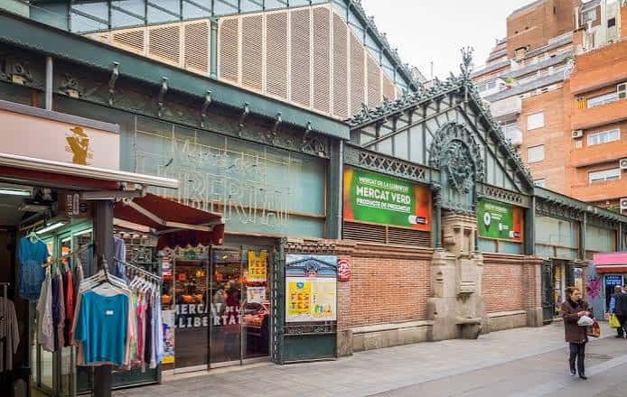 Vista exterior del mercado mostrando su estructura metálica y entrada con letreros informativos