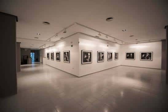 Sala de exposiciones con paredes blancas y obras enmarcadas bajo iluminación profesional
